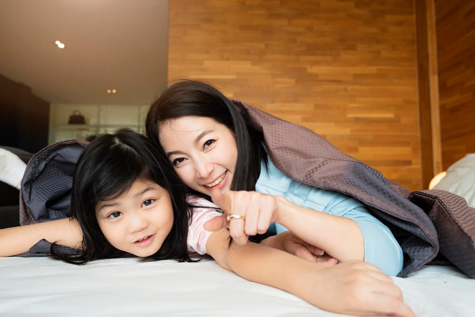 自宅のベッドで寄り添うアジア人の母親と幼い娘